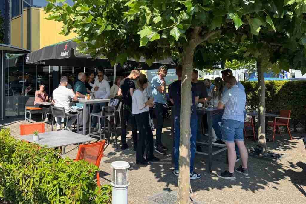 Een groep mensen is gezellig aan het borrelen op een zonnig terras
