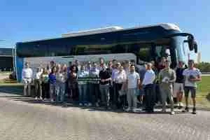 Een groep mensen poseert voor een touringcar op een zonnige dag