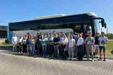 Een groep mensen poseert voor een touringcar op een zonnige dag