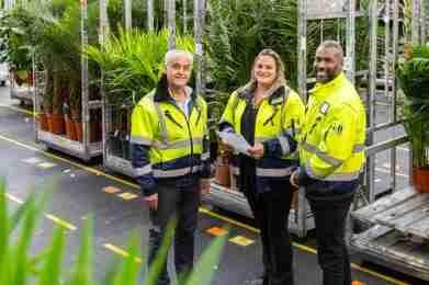 Foto van drie mensen met een gele jas voor een kar met bloemen