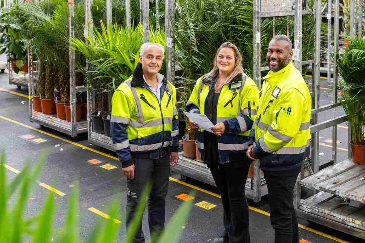 Foto van drie mensen met een gele jas voor een kar met bloemen